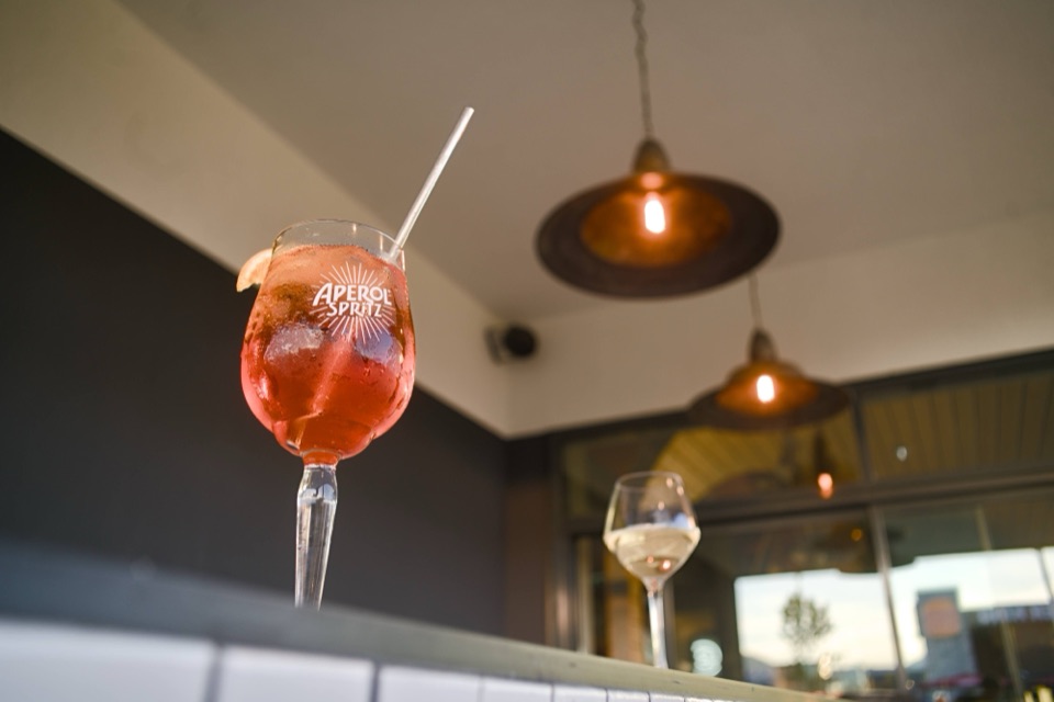 Aperol Spritz en contre-plongée au bar, suspensions cuivrées et lumière du soir