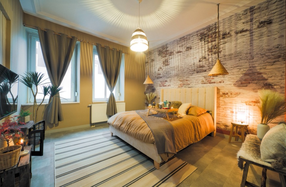 Chambre au mur de briques patinées, tête de lit beige et lumières chaudes