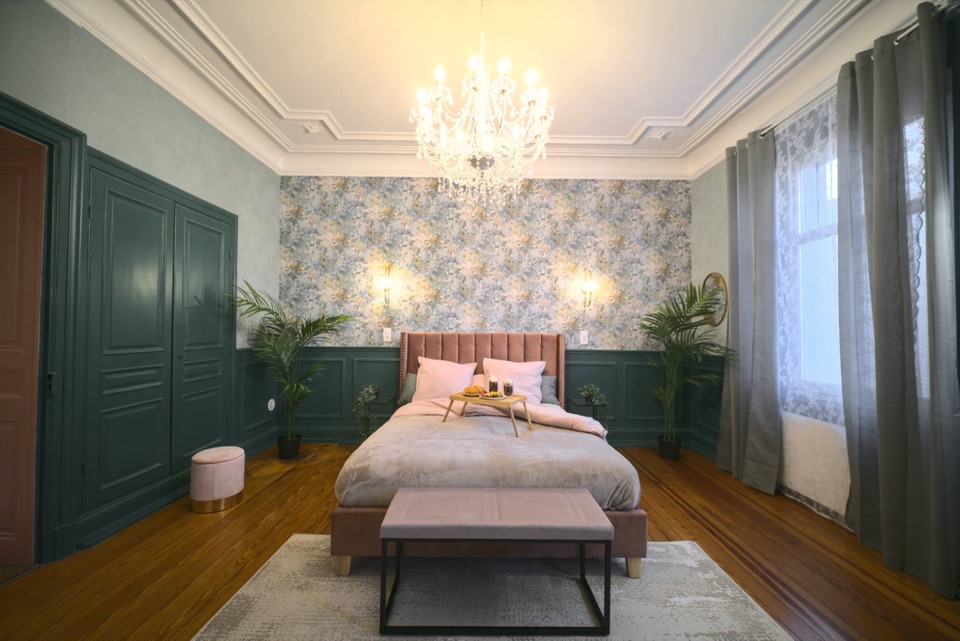 Chambre de maison de maître avec lustre en cristal, moulures et tête de lit velours rose
