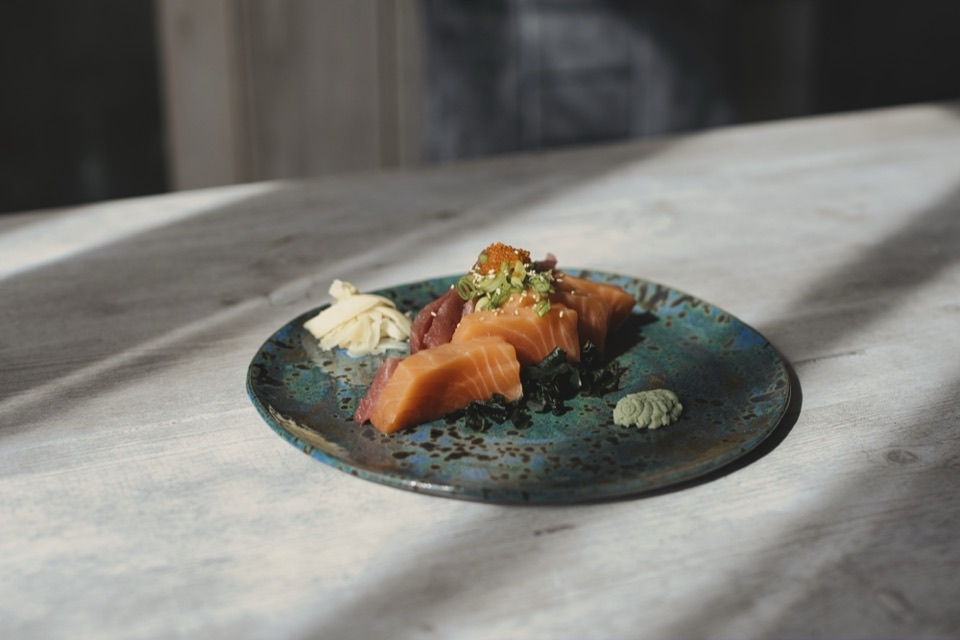 Sashimis de saumon sur une assiette bleue mouchetée, lumière rasante
