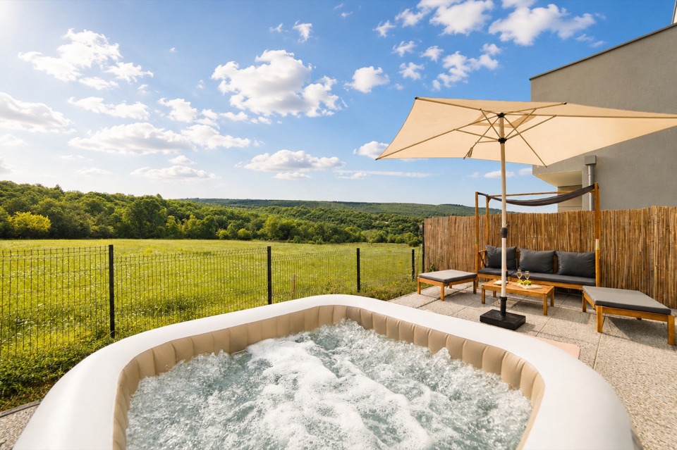 Jacuzzi extérieur en activité sous un ciel bleu, parasol et prairie