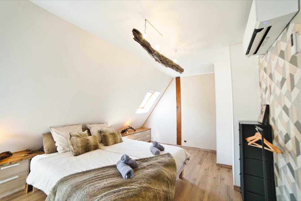 Chambre mansardée avec plaid en fourrure, fauteuil et fenêtre de toit
