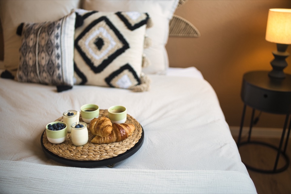 Chambre beige avec coussins à motifs ethniques et plateau de petit déjeuner