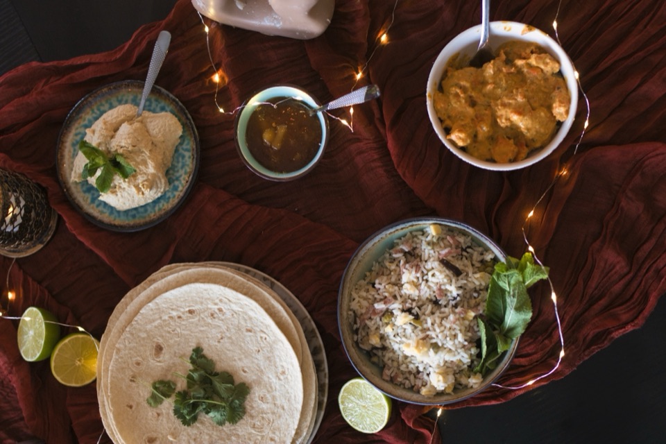 Dîner indien dressé sur un chemin de table rouge avec bougies et guirlande lumineuse, vu de dessus