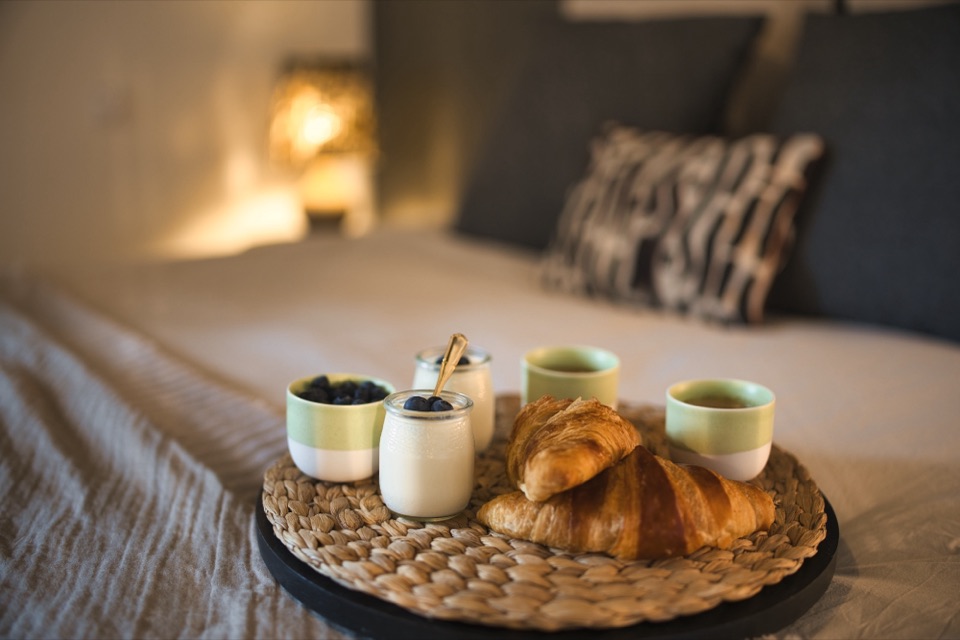 Plateau de petit déjeuner avec croissants et bols posé sur un lit beige