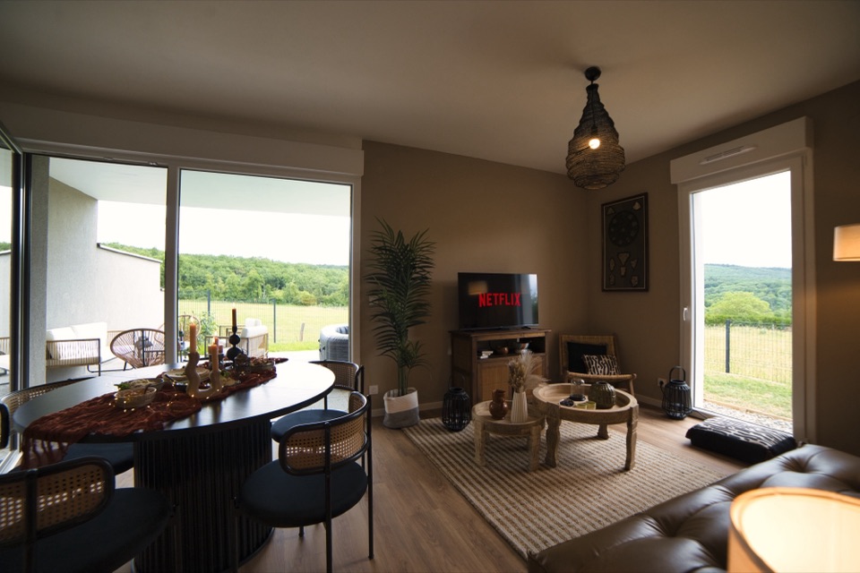 Salon et cuisine ouverte d'un lodge le soir, suspensions allumées, baie vitrée sur la campagne
