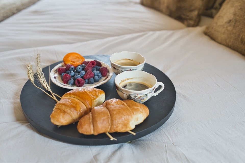 Plateau de petit déjeuner avec croissant, fruits rouges et café posé sur un lit blanc