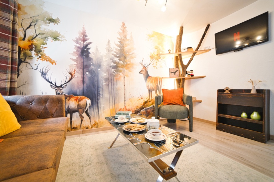 Salon avec fresque de forêt et cerfs, canapé en cuir et coussins orange