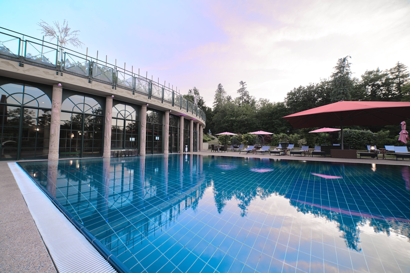 Piscine extérieure d'un hôtel spa 4 étoiles en Alsace au crépuscule, ciel rose reflété dans l'eau