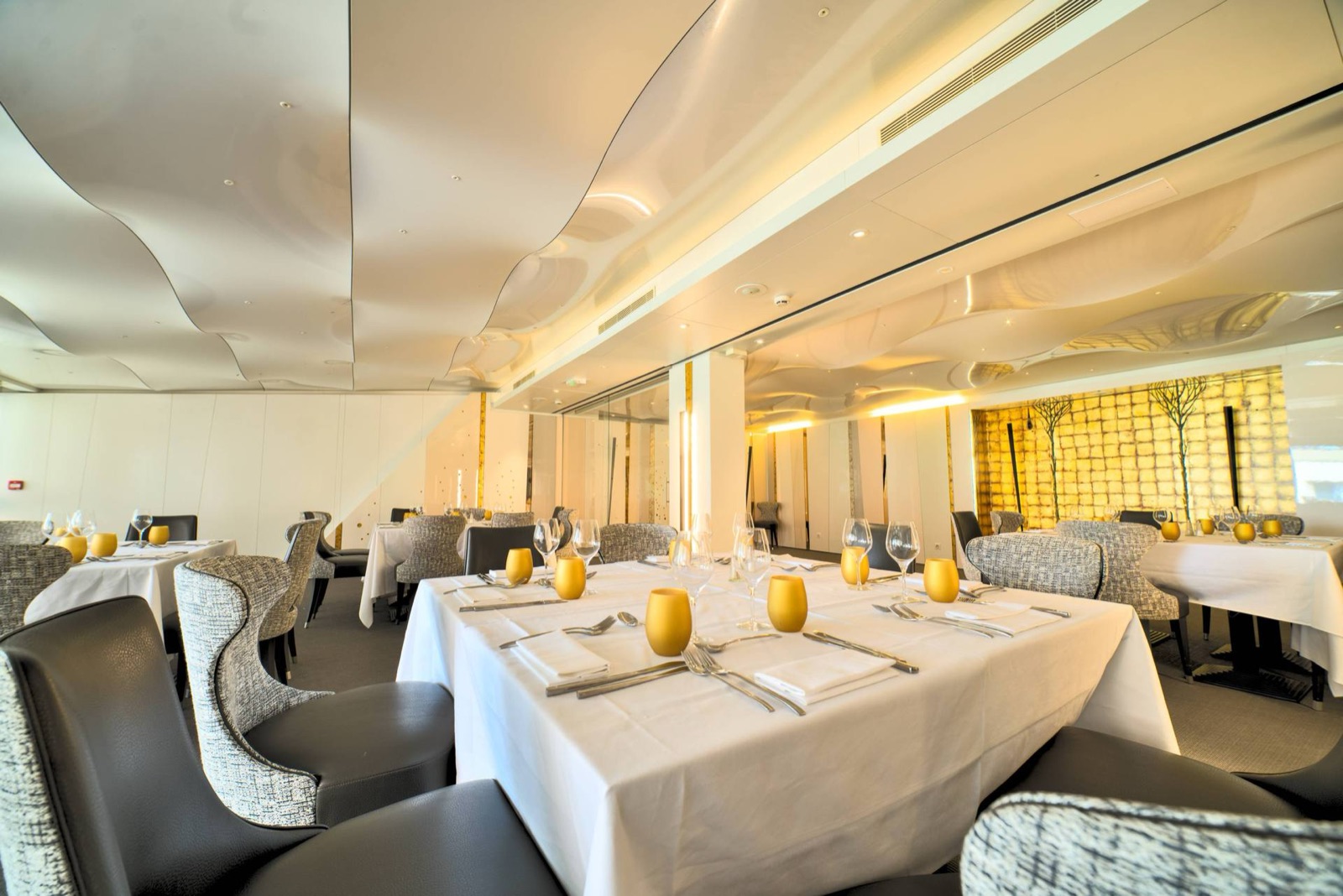 Salle de restaurant gastronomique d'hôtel au plafond sculptural, tables nappées et touches dorées