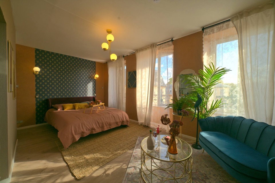 Suite d'hôtel art déco baignée de lumière dorée, lit terracotta et canapé bleu