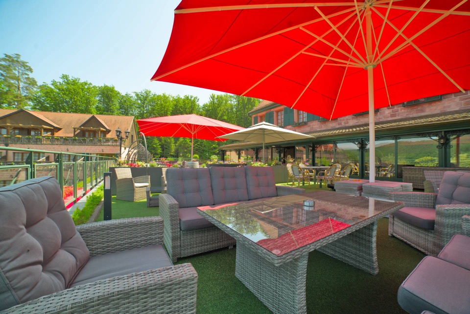 Terrasse lounge d'hôtel avec salons en résine tressée sous grands parasols rouges